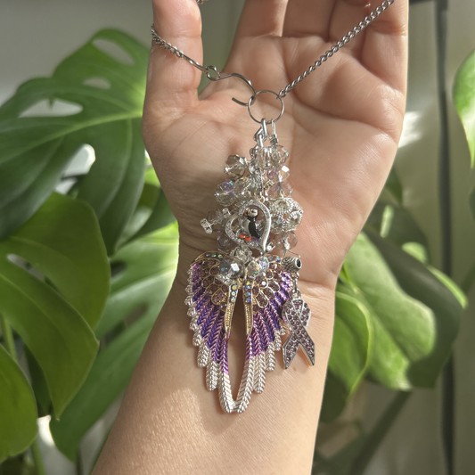 Decorative necklace with purple and silver elements held by a hand against a green leafy background
