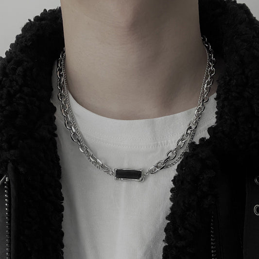 Person wearing a silver chain necklace with a black pendant, dressed in a black cardigan and white shirt.