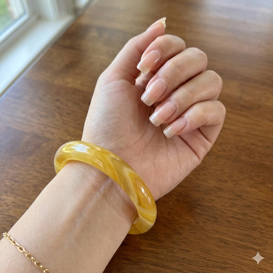Hand wearing a yellow bangle on a wooden surface